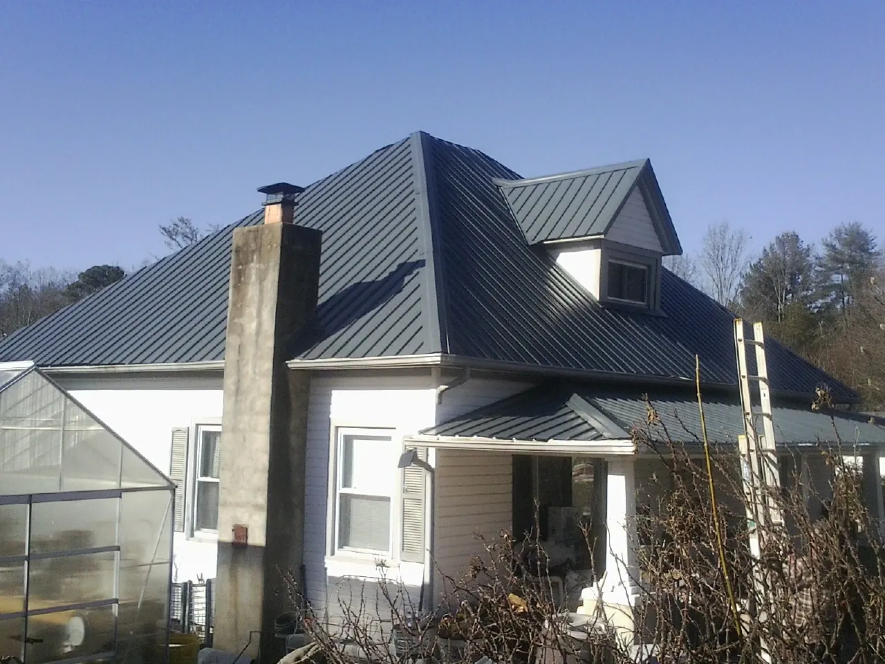 Dark blue standing seam metal roof on a white farmhouse with dormer — Slate & Tile Roof Repair by Roofing Brothers in Trezevant