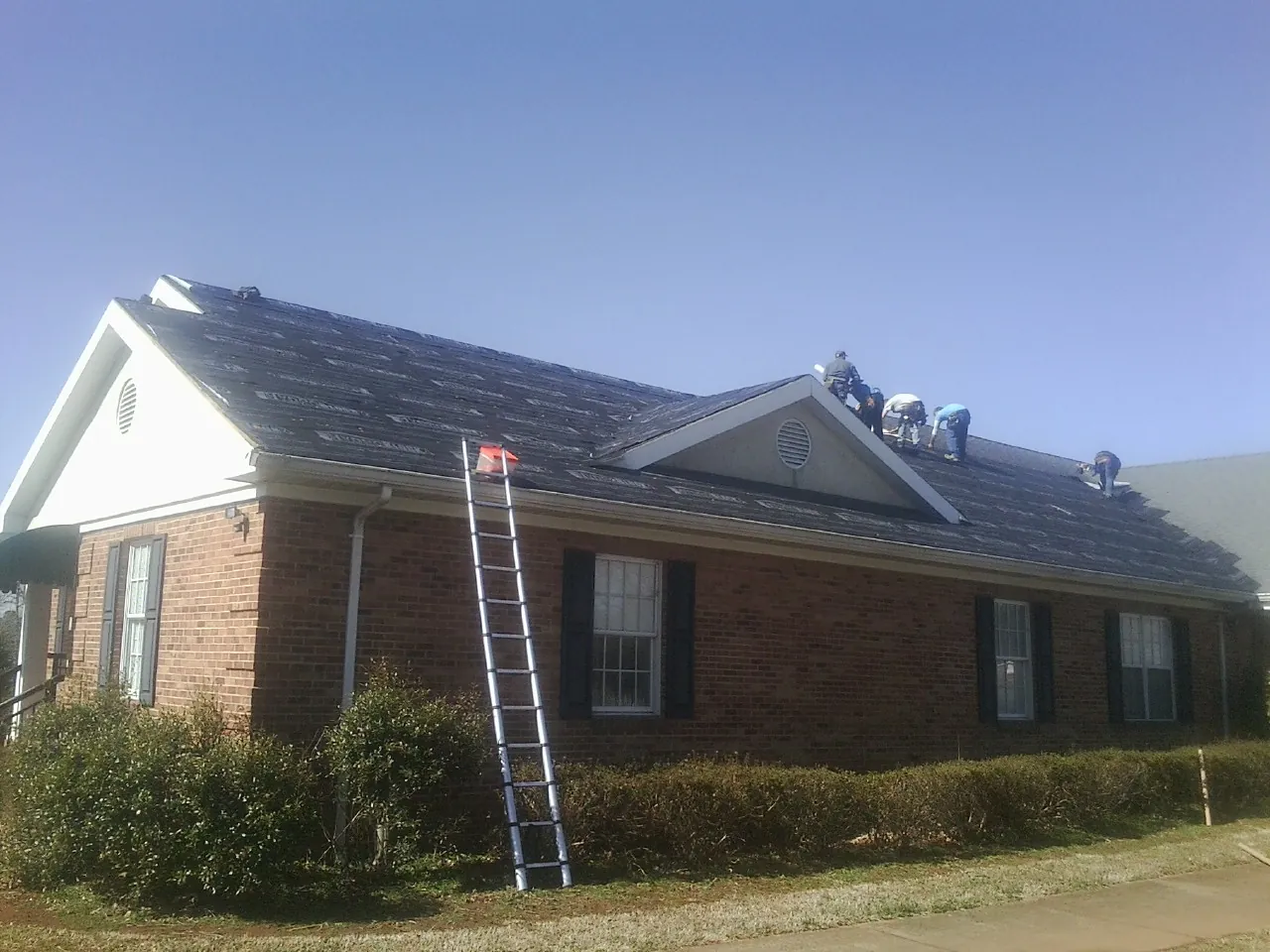Crew tearing shingles off a brick ranch roof with a ladder set — Emergency Roof Repair work by our crew in Trezevant