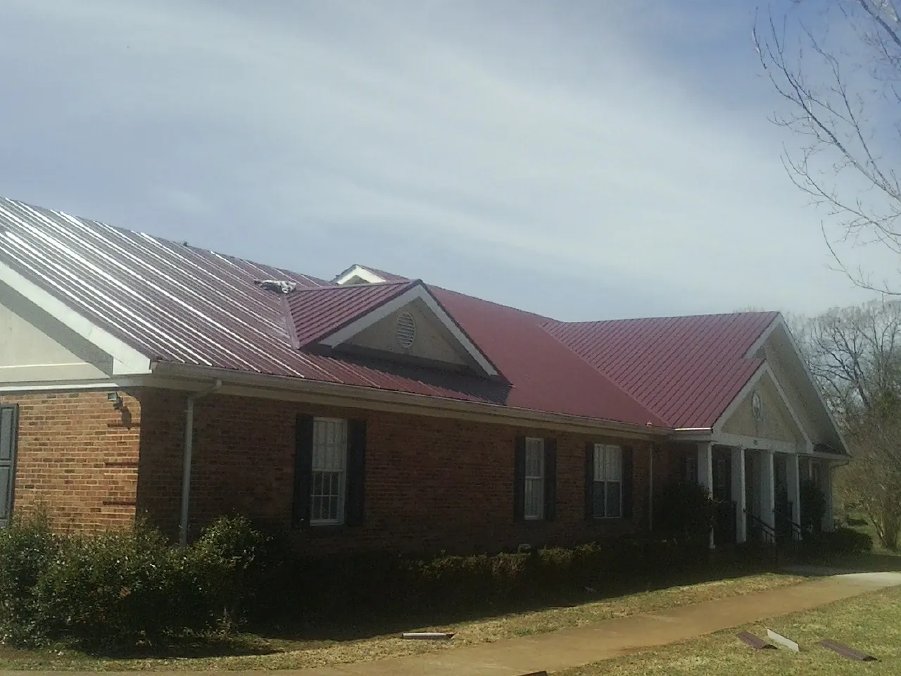 Red metal roof with gabled entries on a long brick building, from a Hail Damage Roof Repair job in Trezevant