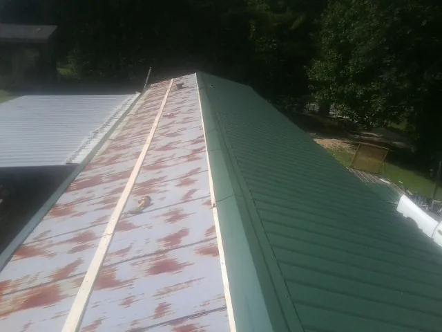 Old rusted panels beside newly installed green metal roofing — Wind Damage Roof Repair by Roofing Brothers in Trezevant