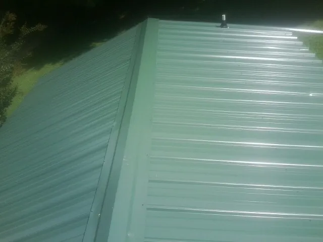 New green metal panels meeting at the ridge of a roof — Flat Roof Repair work by our crew in Trezevant