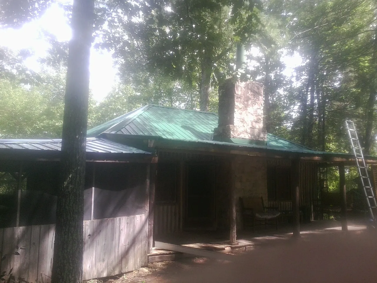 Green metal roof and stone chimney above a log cabin porch in Trezevant
