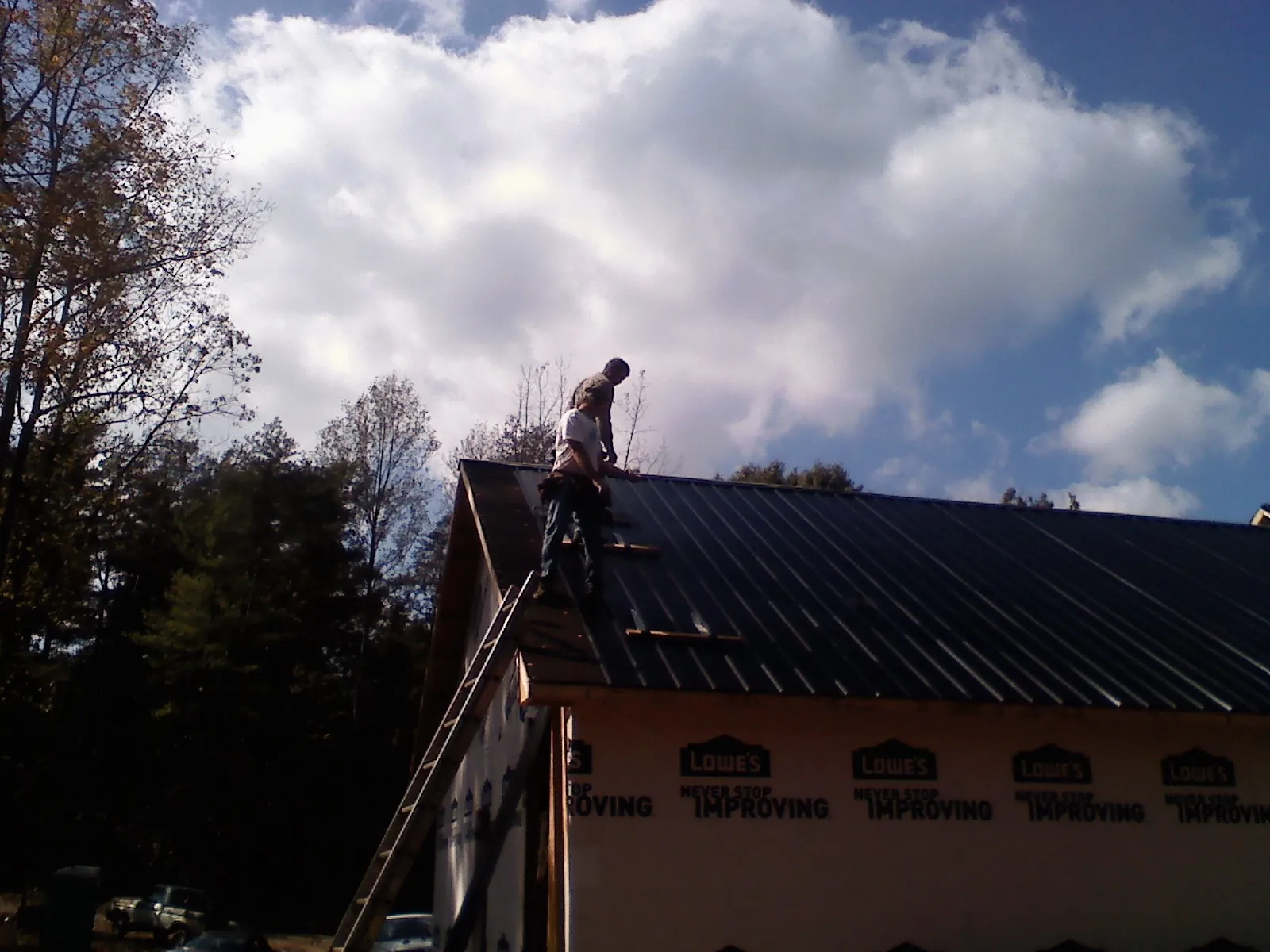 Roofer fastening dark metal panels high against a cloudy sky, from a Roof Inspection job in Trezevant
