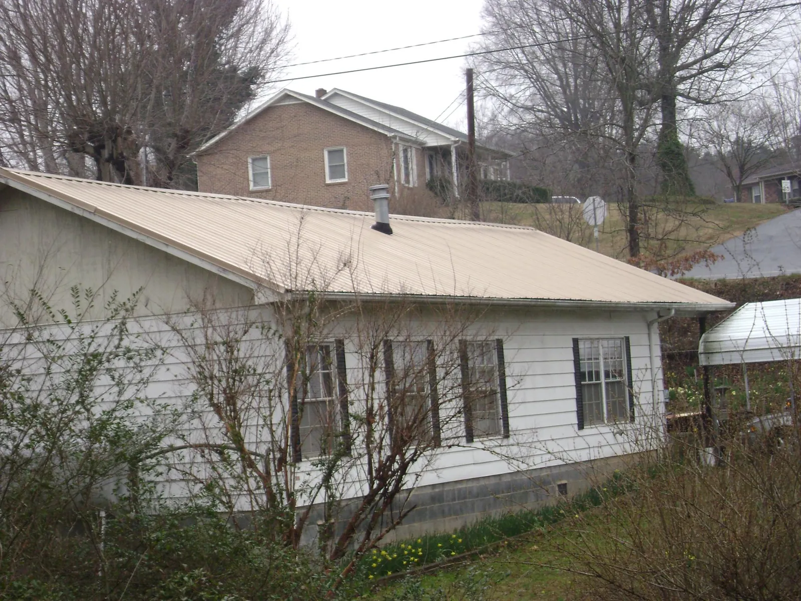 Tan metal roof on a white sided house set into a hillside — Commercial Roofing by Roofing Brothers in Trezevant